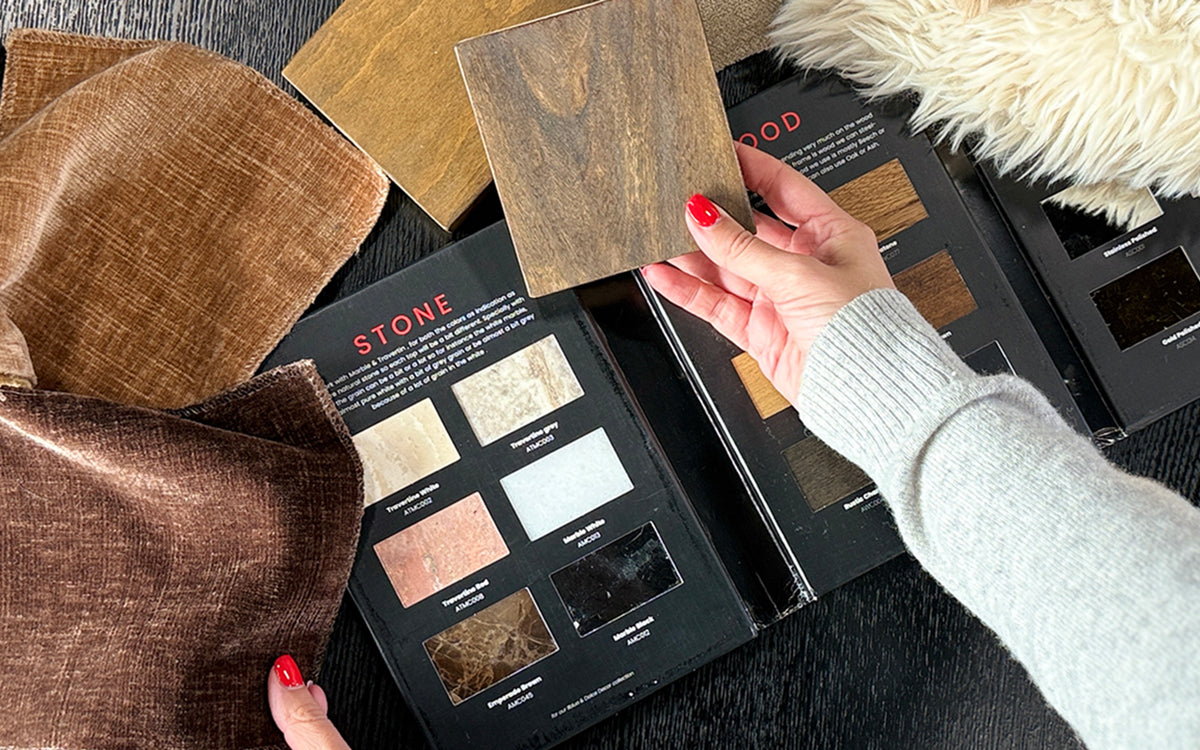 Hand holding a wood sample above a fabric swatch and a color palette with stone and wood options on a dark surface.